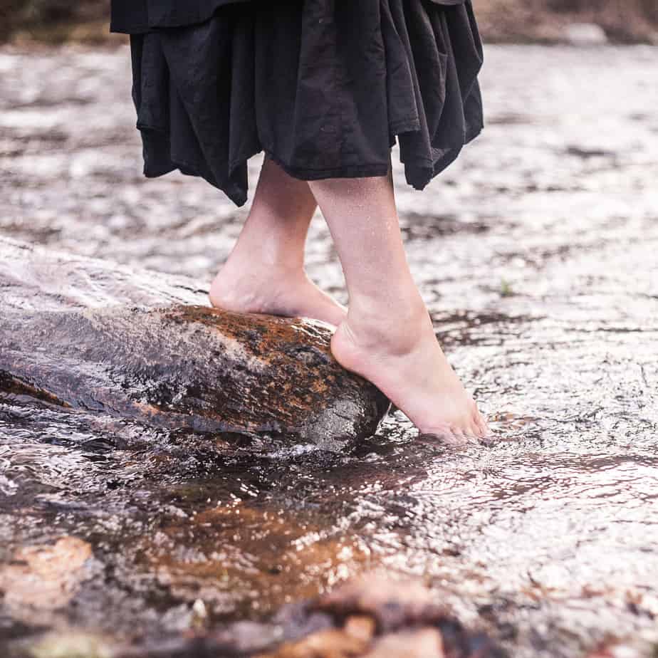 Maia dipping her foot in the river while standing on a rock.